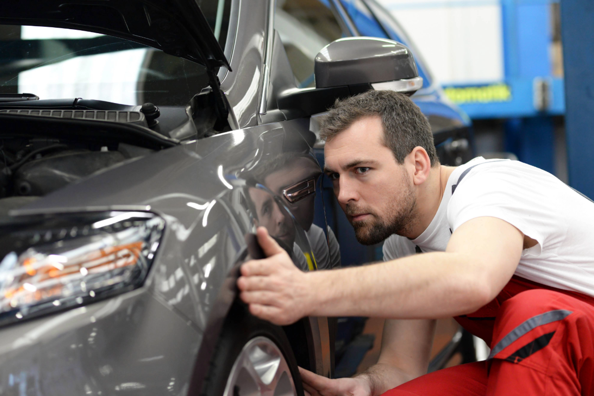 zu sehen ist ein KFZ Mitarbeiter, der den Lack des Autos überprüft